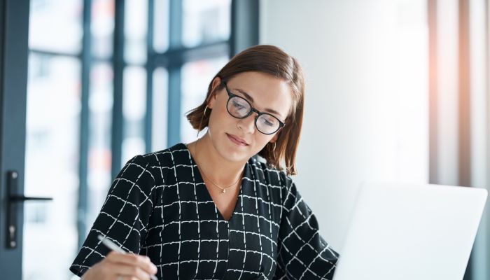 Woman sitting in front of laptop, writing in journal